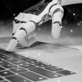 A robot hand types on a computer keyboard